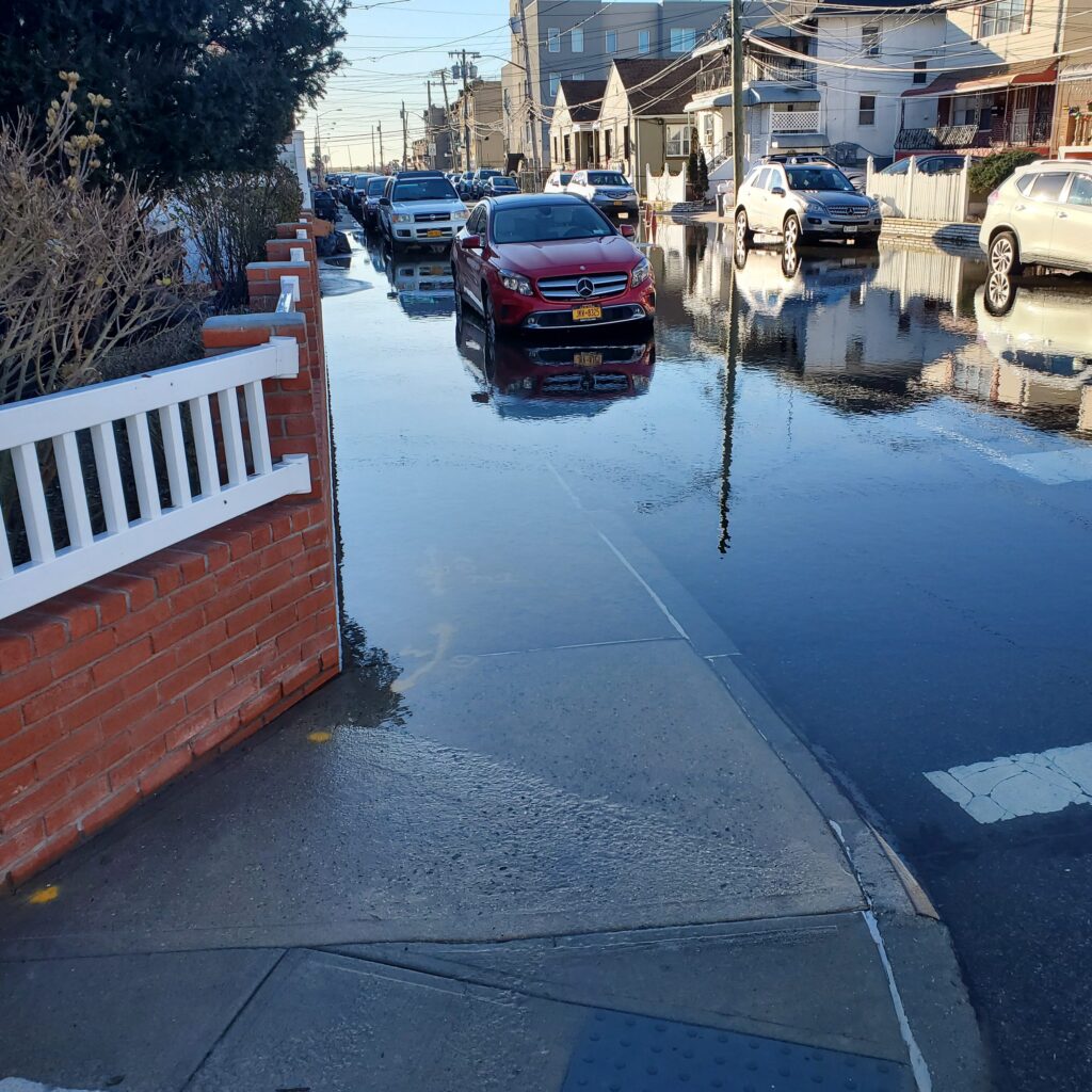 a street with cars parked on the side and a building with a puddle (MyCoast AI)