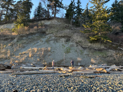 a couple people standing on a rocky hillside with trees and blue sky (MyCoast AI)