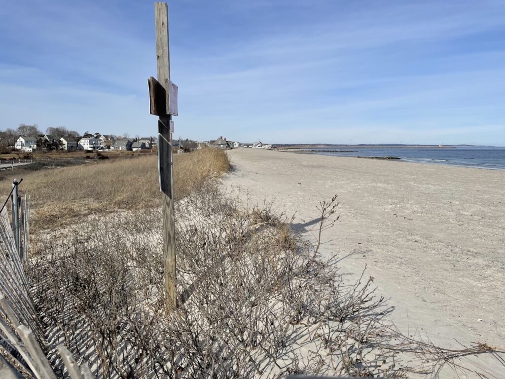 a beach with a fence and a pole with a sign on it (MyCoast AI)